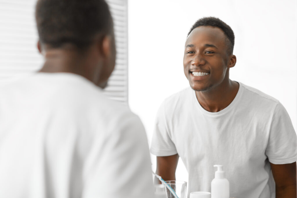 Black Man Smiling Looking At His Teeth In Mirror Indoors