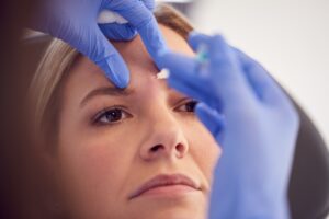 Woman Sitting In Chair Being Give Botox Injection Between Eyes By Female Doctor