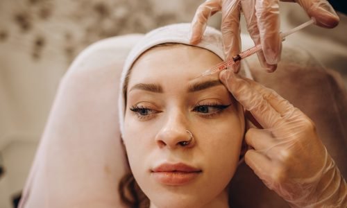 Portrait of young Caucasian woman getting botox cosmetic injection in forehead. Beautiful woman gets